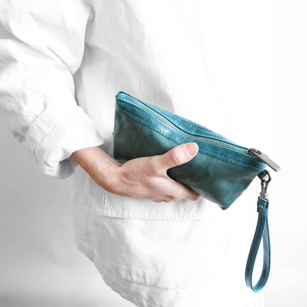 Close-up of model holding a zip pouch medium in rodeo teal and tourmaline.
